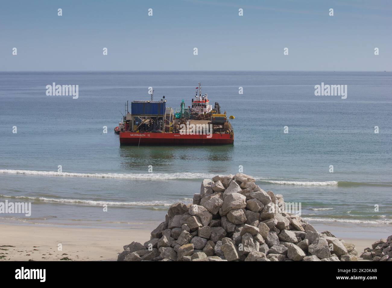 Armures déchargées pour construction brise-lames Coverack Bay avec barge de transport. Banque D'Images