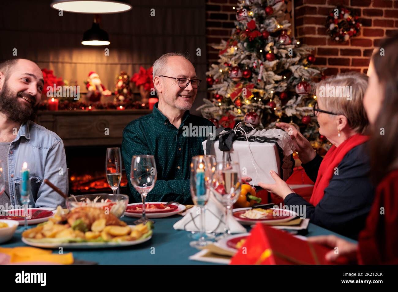 Famille célébrant noël, échanger des cadeaux à table festive, manger des plats traditionnels à la maison. Fête de Noël avec les parents, les personnes donnant des boîtes de cadeau Banque D'Images