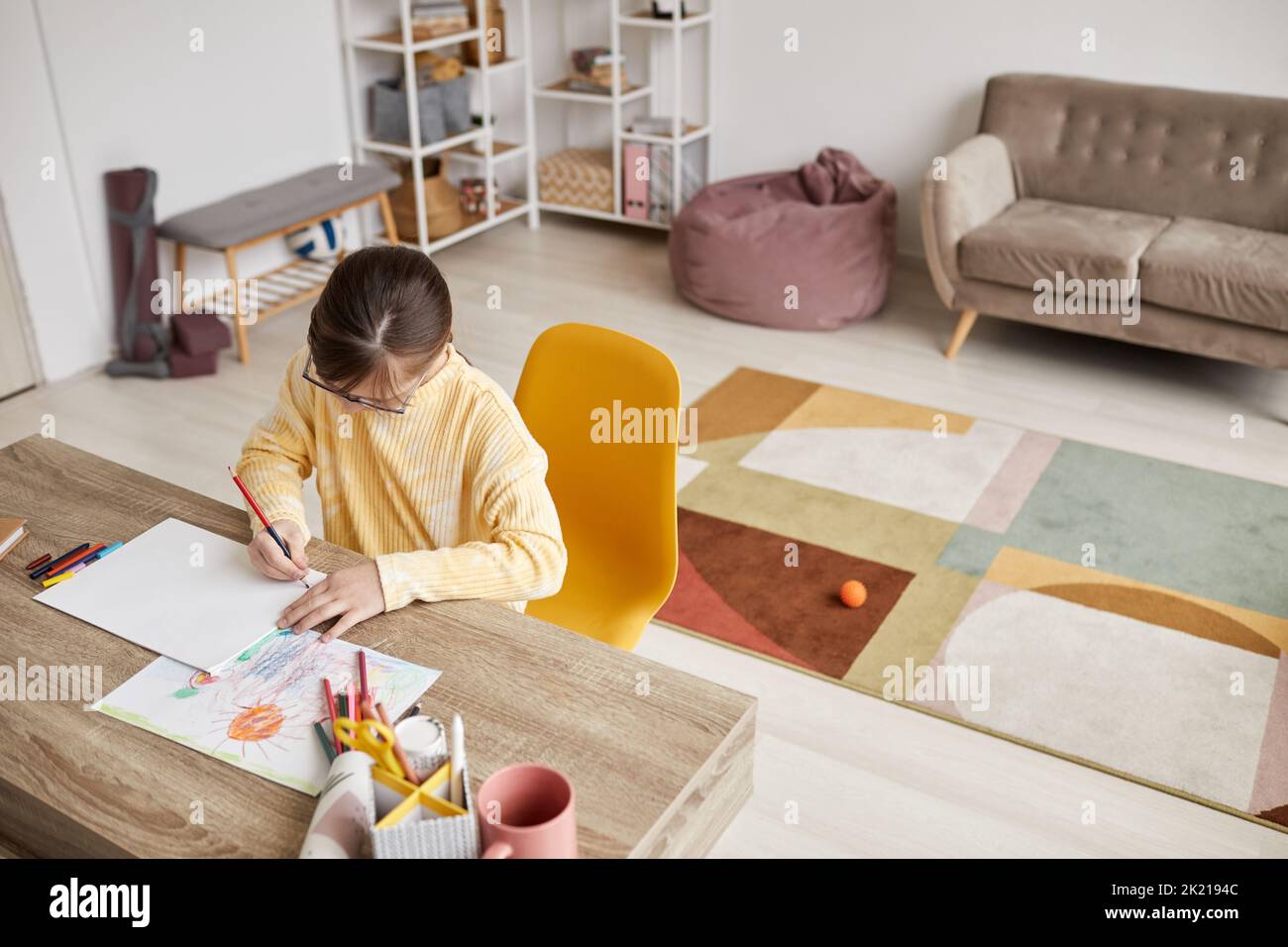 Mini portrait grand angle de la jeune fille dessin des images à la table dans la pièce confortable, espace de copie Banque D'Images