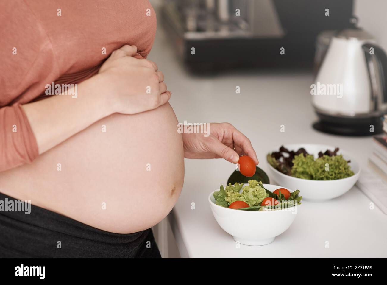 Faire le choix sain pour bébé et moi. Une jeune femme enceinte qui mange une salade dans la cuisine. Banque D'Images