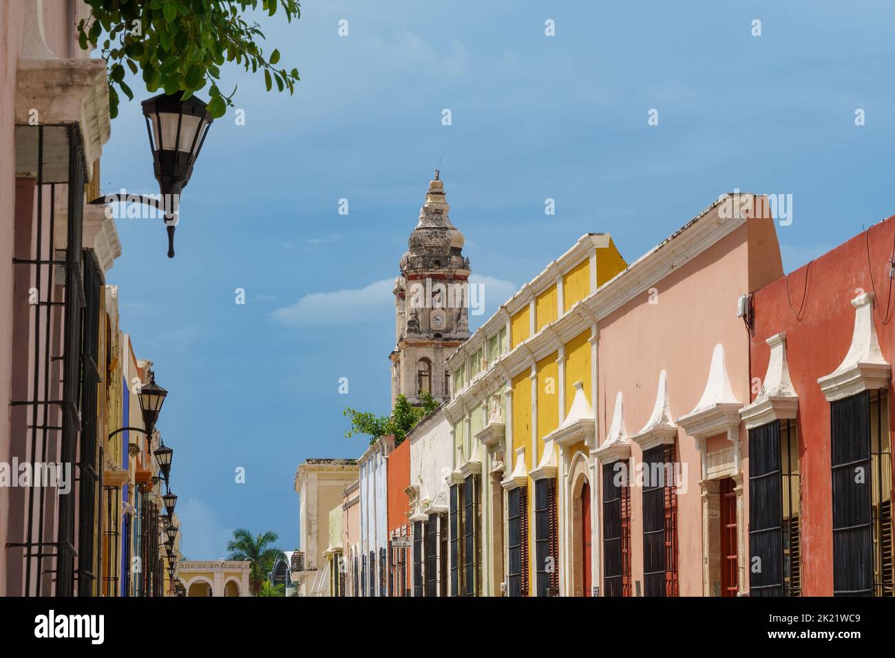 De vieux bâtiments colorés et des lampes de rue bordent une rue avec une tour d'église émergeant au-dessus - à Campeche, au Mexique Banque D'Images