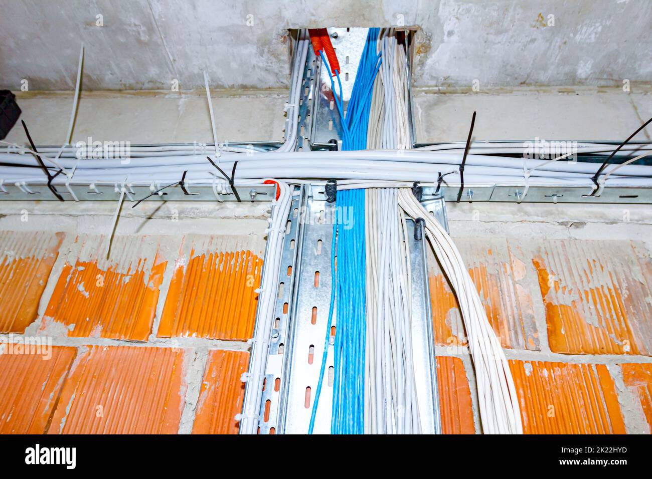 Un plateau perforé en métal avec faisceau de câbles isolés passe entre les sols à travers un trou quadratique de plafond dans un bâtiment en construction. Banque D'Images