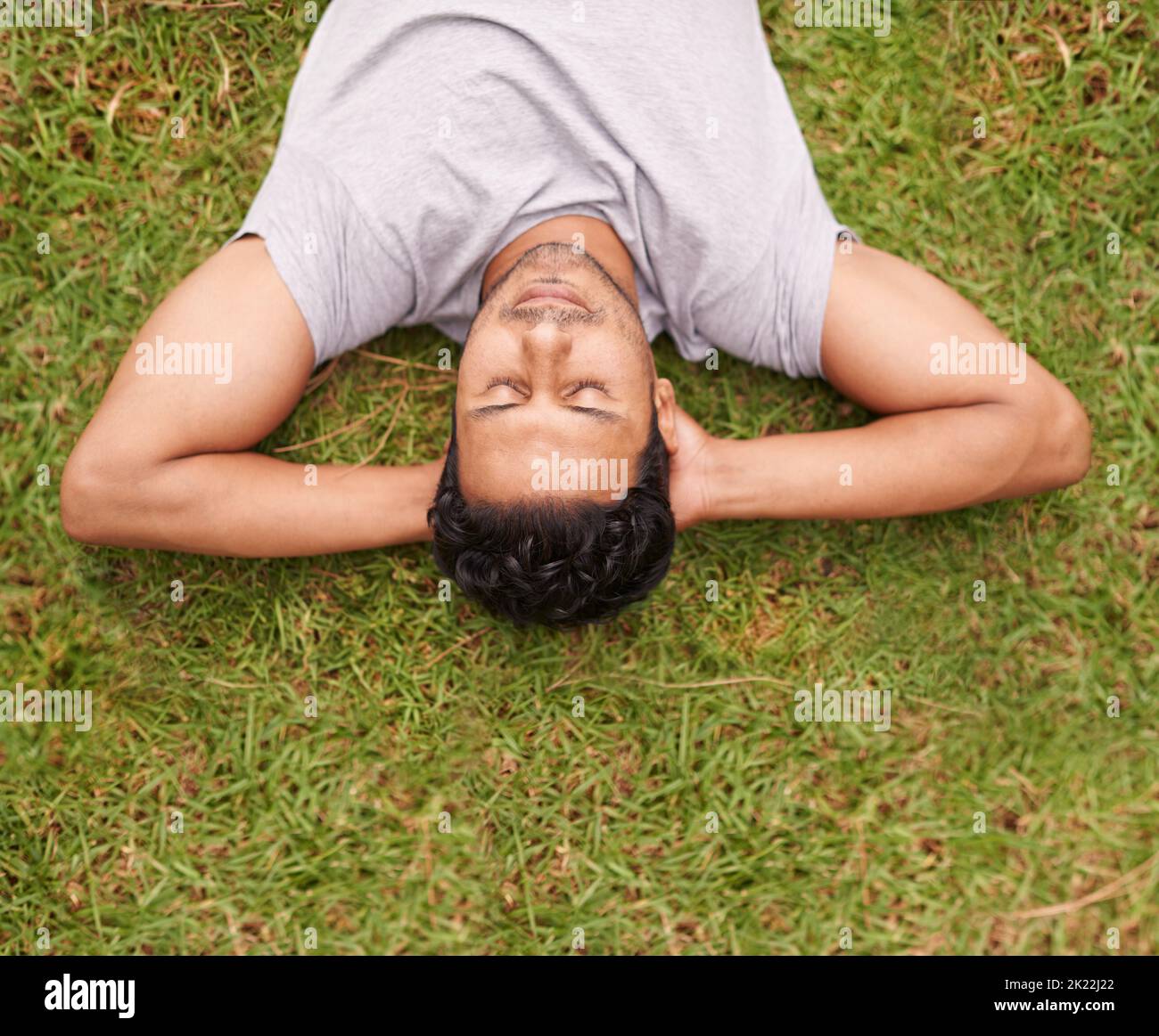 Prenez le temps de vous détendre. Un jeune homme allongé sur l'herbe avec ses mains derrière sa tête. Banque D'Images