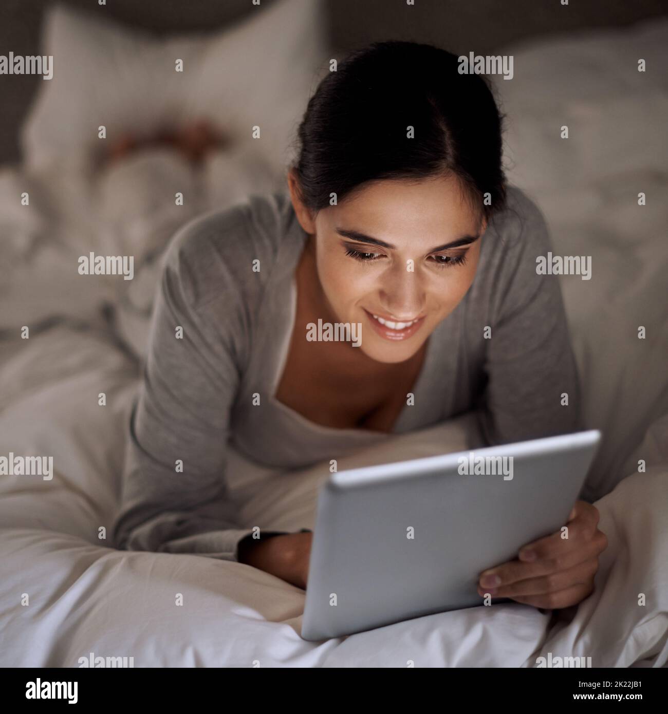 Réseau nocturne. Une jeune femme attrayante utilisant sa tablette dans le lit. Banque D'Images