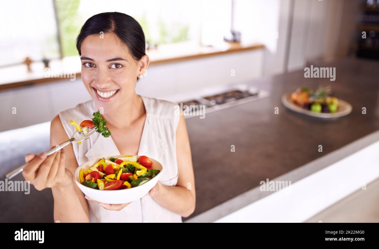 Ma santé est ma richesse. Jeune femme appréciant une salade en se tenant dans sa cuisine Banque D'Images