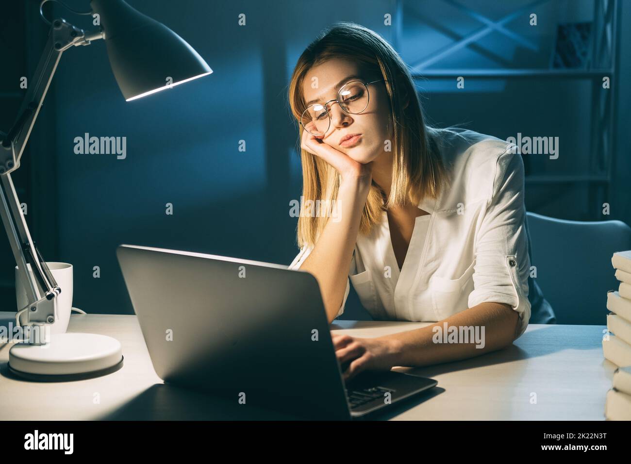Travailler à domicile. Verrouillez vos activités. Femme fatiguée et ennuyeuse travaillant sur un ordinateur portable dans un espace de travail sombre Banque D'Images