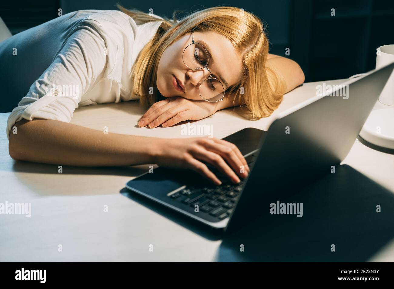 Fatigue du travail excessif. Date limite de la tâche. Charge de travail non saine. Une femme fatiguée, épuisée, dormant sur un ordinateur portable dans un bureau sombre Banque D'Images
