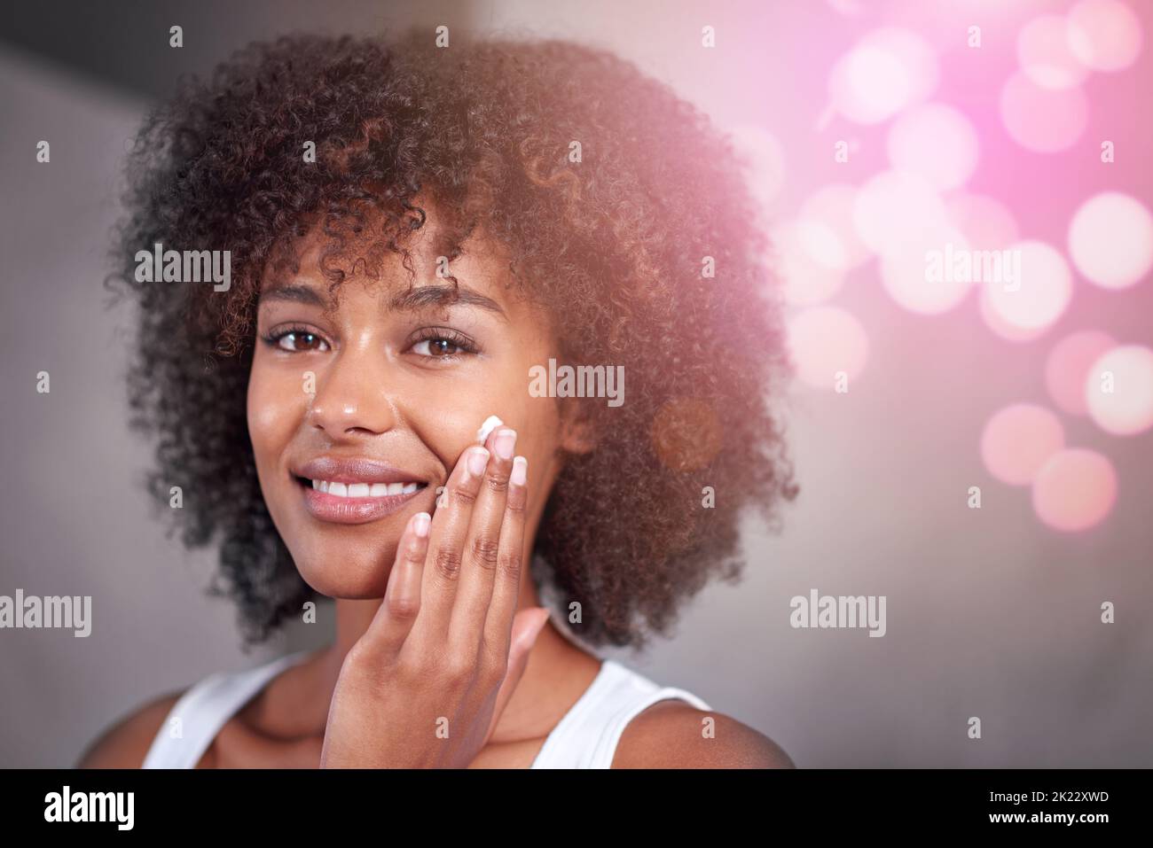 Je vous parle de soin de la peau. Portrait court d'une jeune femme hydratant son visage dans la salle de bains Banque D'Images