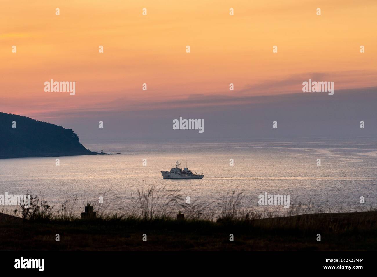 Superbe paysage au coucher du soleil avec un bateau, isolé, près du continent, dans une baie. Ciel orange et violet. Réflexions du ciel sur l'eau Banque D'Images