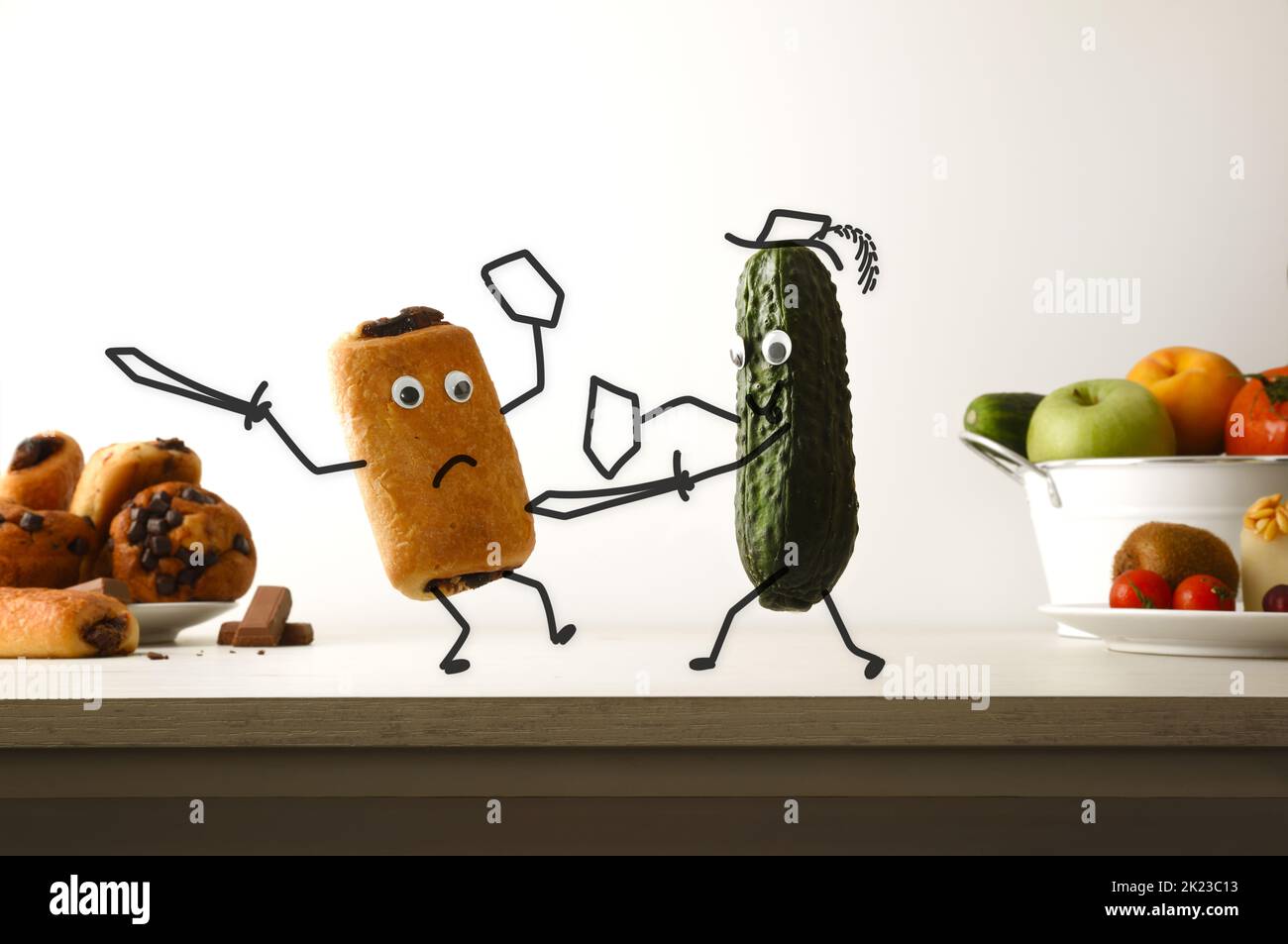 Healthy eating and unhealthy food concept with cucumber battling chocolate muffin on kitchen bench with isolated background. Front view. Banque D'Images