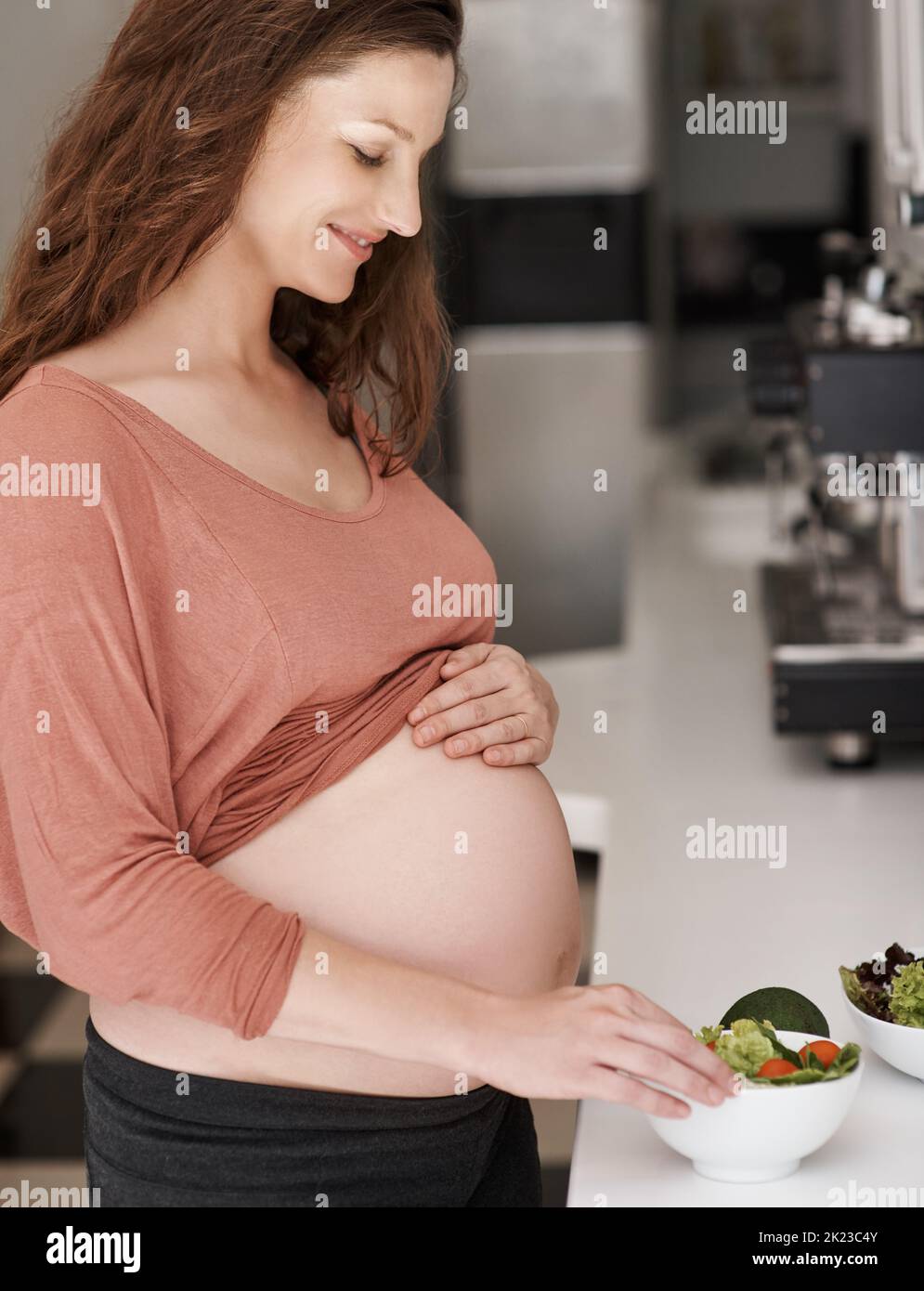 Il faut manger sainement quand vous êtes enceinte. Une jeune femme enceinte mange une salade dans la cuisine. Banque D'Images