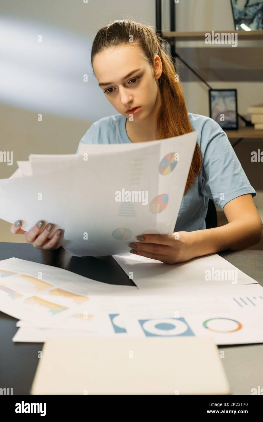 Vérification de la responsabilisation. Travailleur indépendant. Travailler à domicile. Femme concentrée assise dans un espace de travail de bureau tard dans la nuit étudiant des papiers avec des graphiques Banque D'Images
