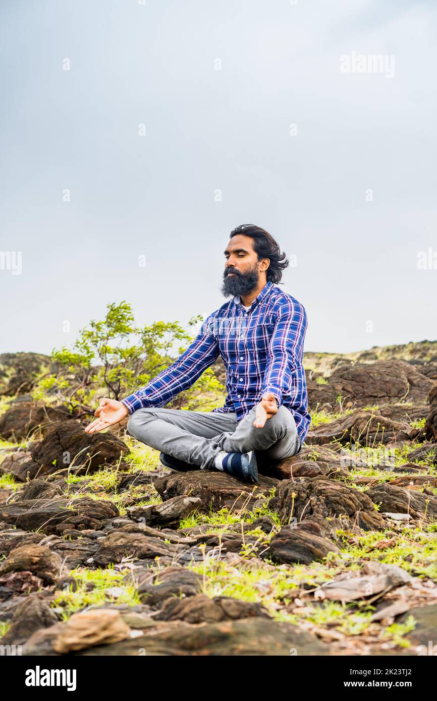 Plan vertical du jeune homme de barbe avec les yeux fermés faire la méditation ou le yoga sur le sommet de la colline - concept de l'auto-soin, des soins de santé et de bien-être Banque D'Images