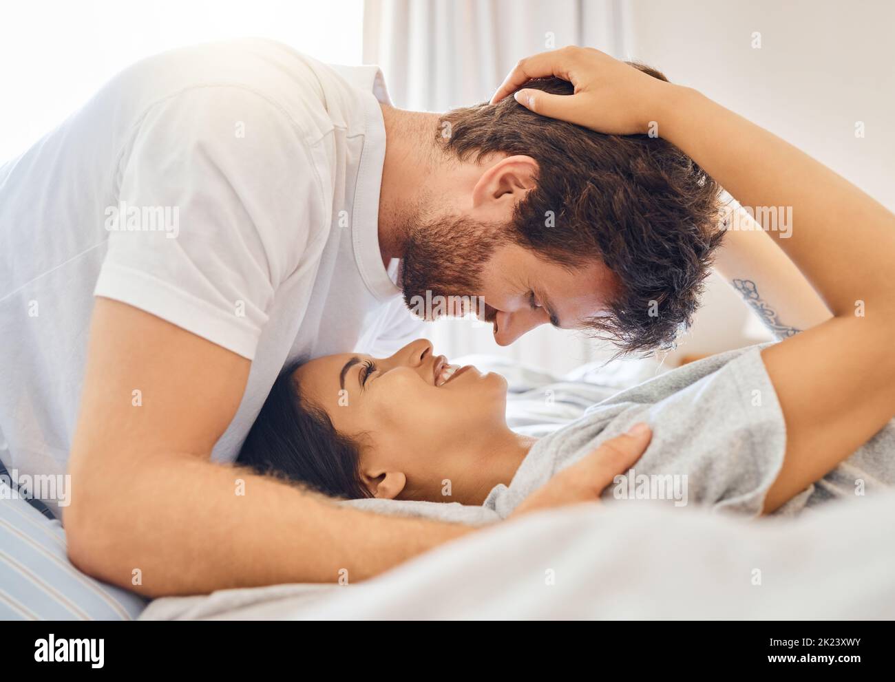 Couple, amour et heureux avec un homme et une femme au lit dans la chambre de leur maison avec un sourire. Romance, datation et affection avec un jeune homme Banque D'Images
