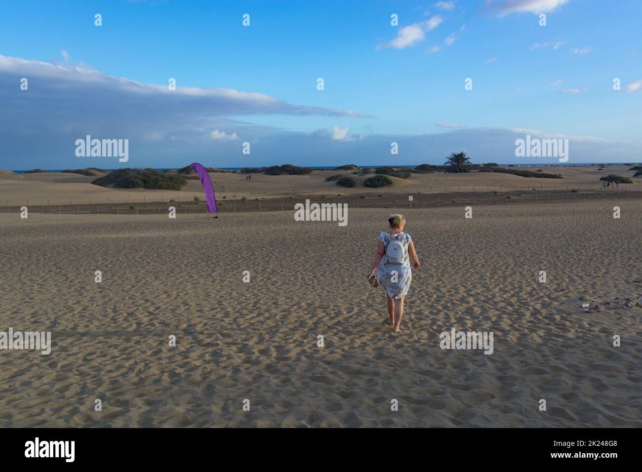 Femme en robe marchant dans le sable des dunes du désert avec des marches dans le sable du désert, jeune femme marchant dans le sable blanc un jour d'été brillant, vacances va Banque D'Images