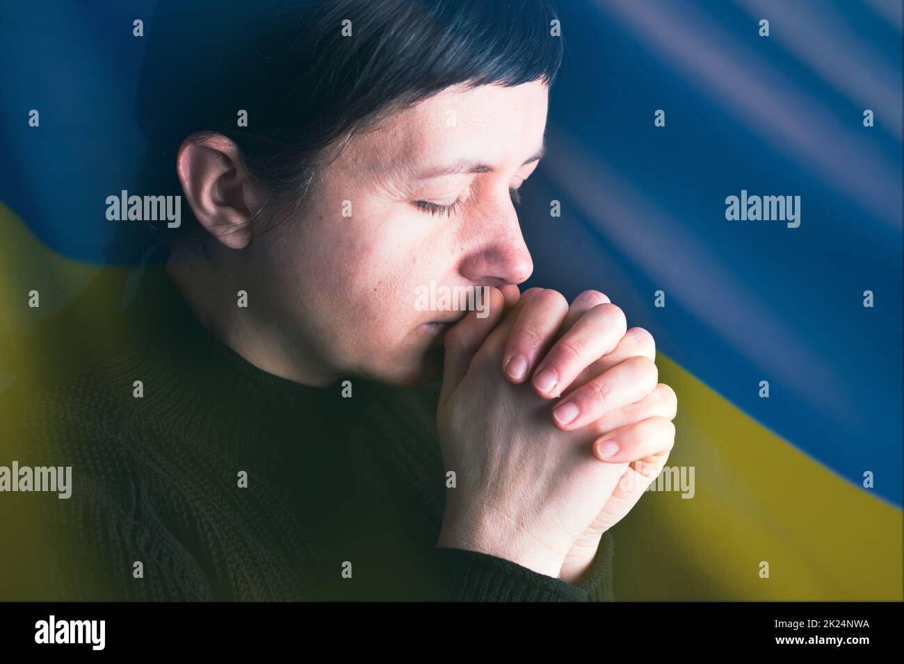 Triste femme avec le drapeau de l'Ukraine en arrière-plan priant. Concept de se tenir debout avec la nation ukrainienne en guerre avec la Russie. Banque D'Images