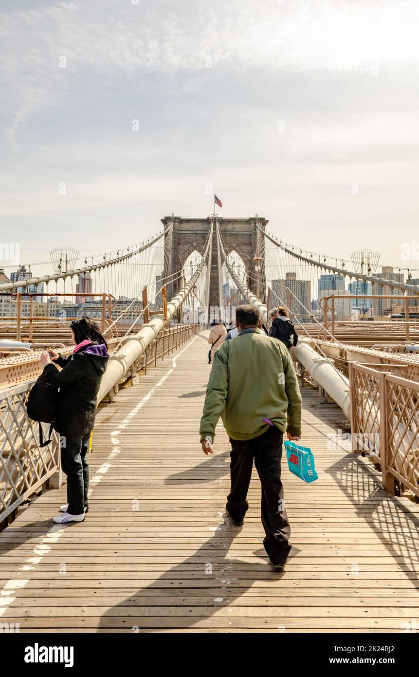 Brooklyn Bridge New York City avec un petit groupe de personnes marchant sur le pont, homme portant la vue arrière, dans la soirée pendant l'hiver, vertical Banque D'Images