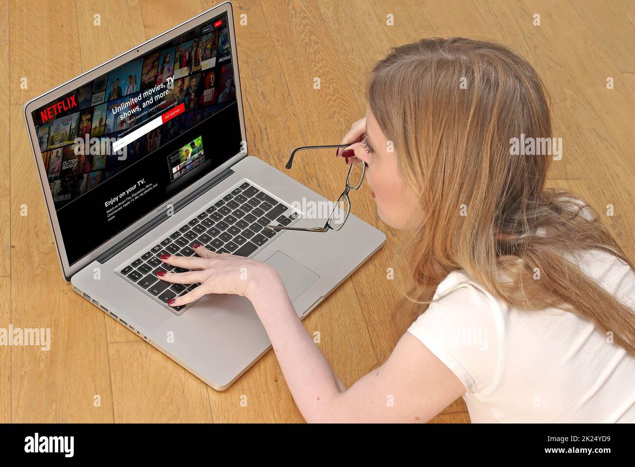 Londres, Royaume-Uni - 13 janvier 2022: Jeune femme sur le sol à la maison en utilisant portable Internet streaming service navigation Netflix page d'accueil choisir m Banque D'Images
