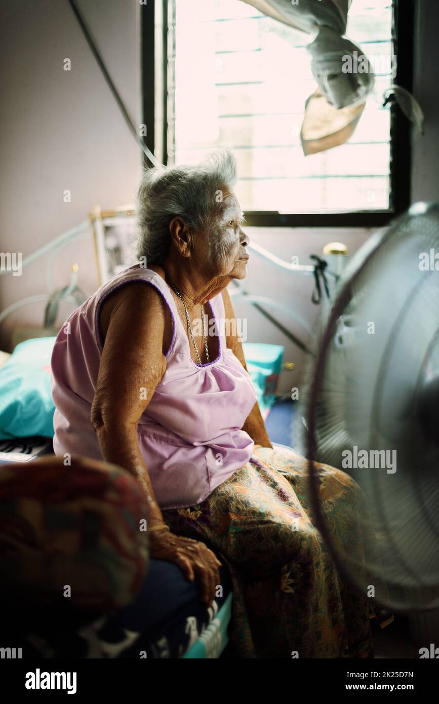 Une femme asiatique à la retraite est assise dans sa chambre, regardant la télévision à la maison. Banque D'Images