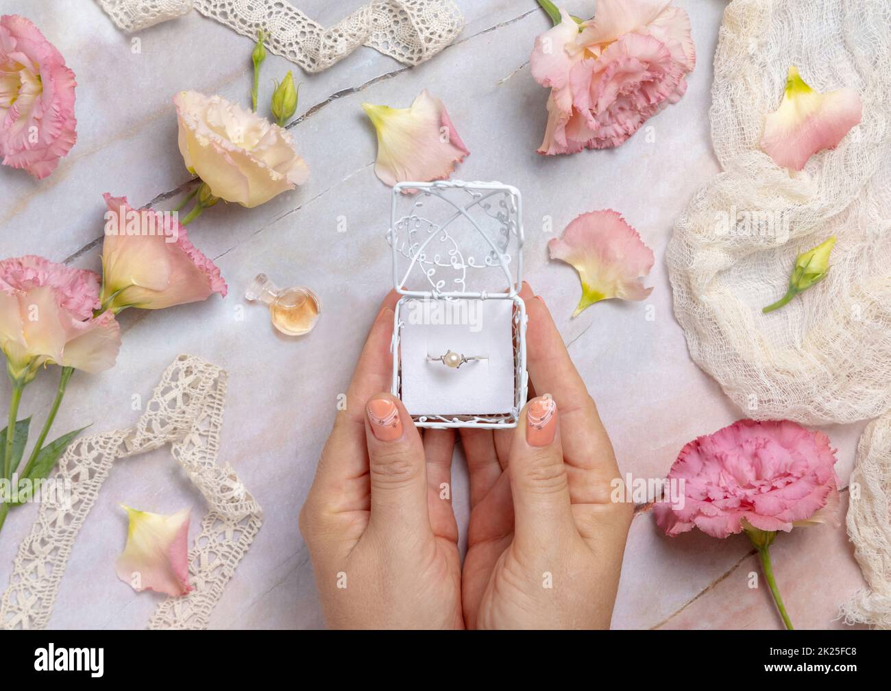 Femme mains tenant une boîte cadeau avec un anneau de perle avec des fleurs rose clair autour Banque D'Images