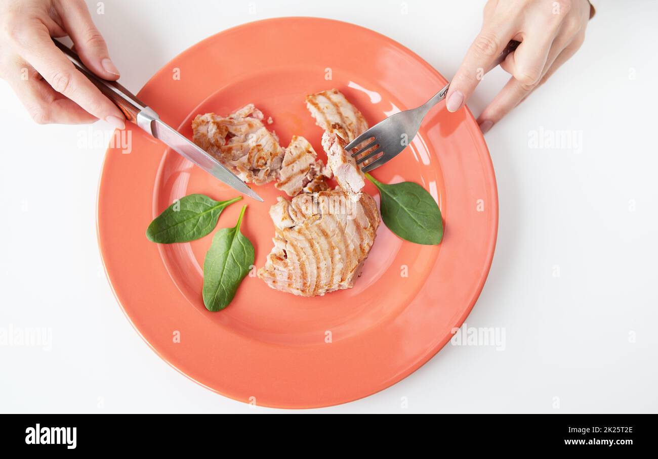 Gros plan d'un délicieux steak de thon grillé juteux sur une assiette de corail vif. Des aliments délicieux et sains, une bonne nutrition. La fille tient une fourchette et un couteau. Vue de dessus. Banque D'Images