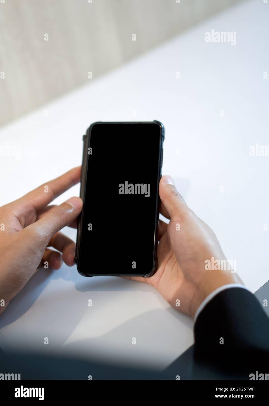 Homme d'affaires en costume noir tenant un écran vierge téléphone portable avec les deux mains. Banque D'Images