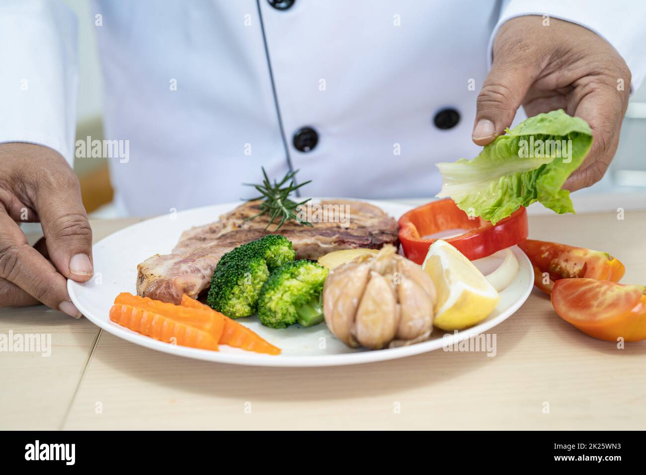 Le chef prépare et prépare une assiette de steak de porc et de salade dans la cuisine de l'hôtel ou du restaurant. Banque D'Images