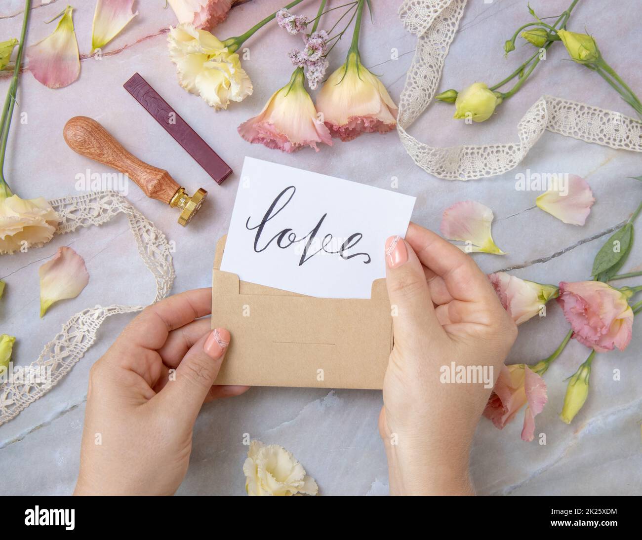 Mains avec carte AMOUR à l'intérieur de l'enveloppe près de fleurs roses sur une table en marbre Banque D'Images