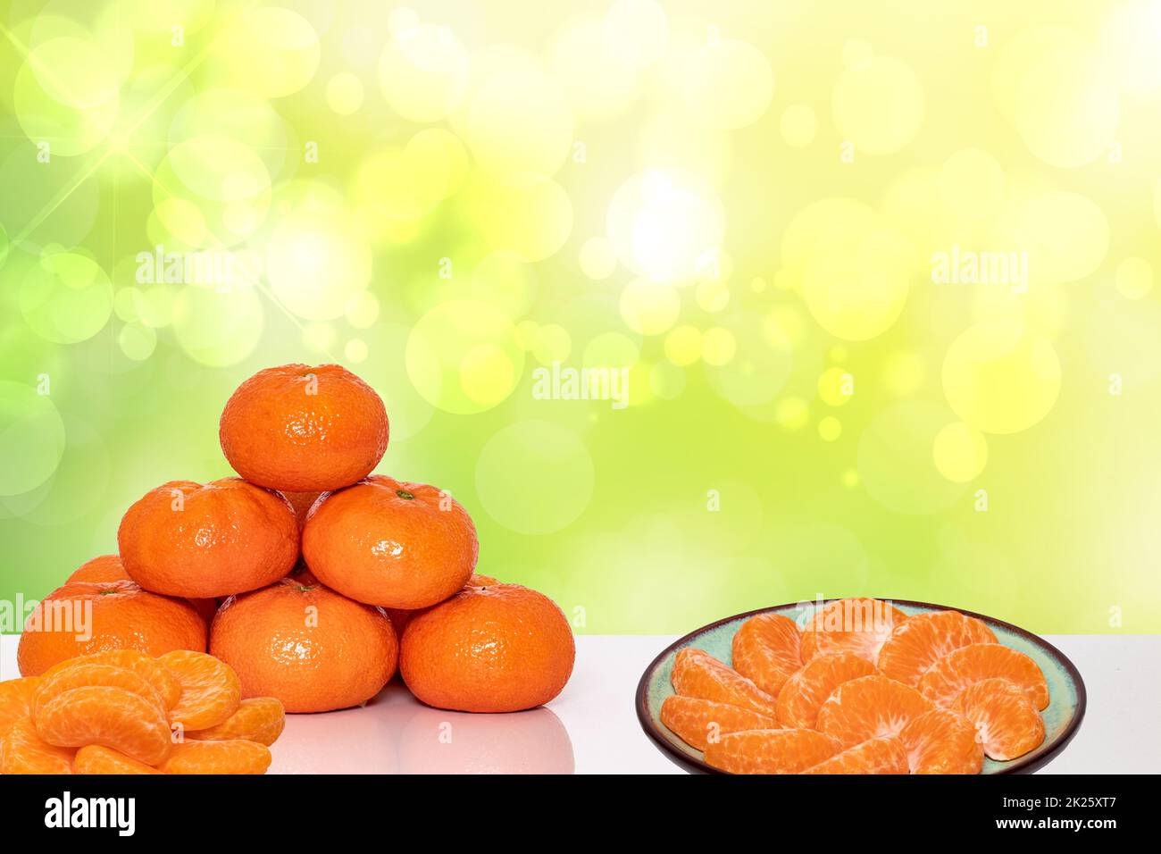 Pile de mandarines mûres fraîches, de mandarines d'agrumes ou d'orangs et de tranches de mandarine pelée sur une assiette sur fond abstrait et lumineux. Espace publicitaire. Clémentines pour la nutrition santé. Banque D'Images