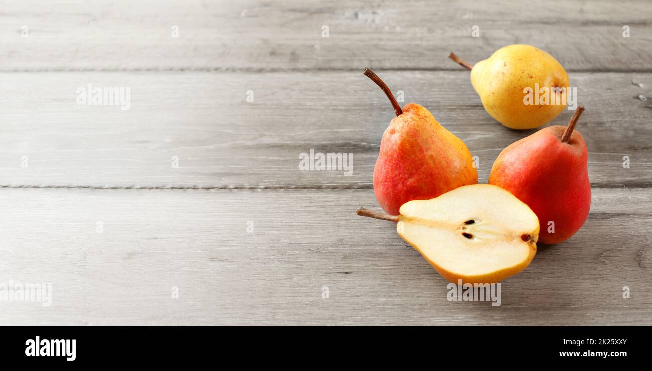 Ensemble de trois fruits rouges et jaunes, poires, et l'un réduit de moitié sur les planches de bois gris. Taille de la bannière avec place pour le texte sur la gauche. Banque D'Images