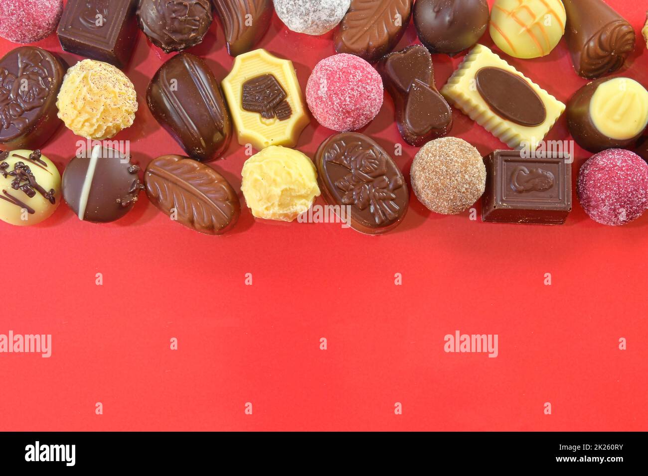 Pralines au chocolat. Bonbons au chocolat sur fond rouge. Cadre chocolat vue de dessus. Arrière-plan de pralines de chocolat avec espace de copie pour le texte. Bordure de différentes friandises Banque D'Images