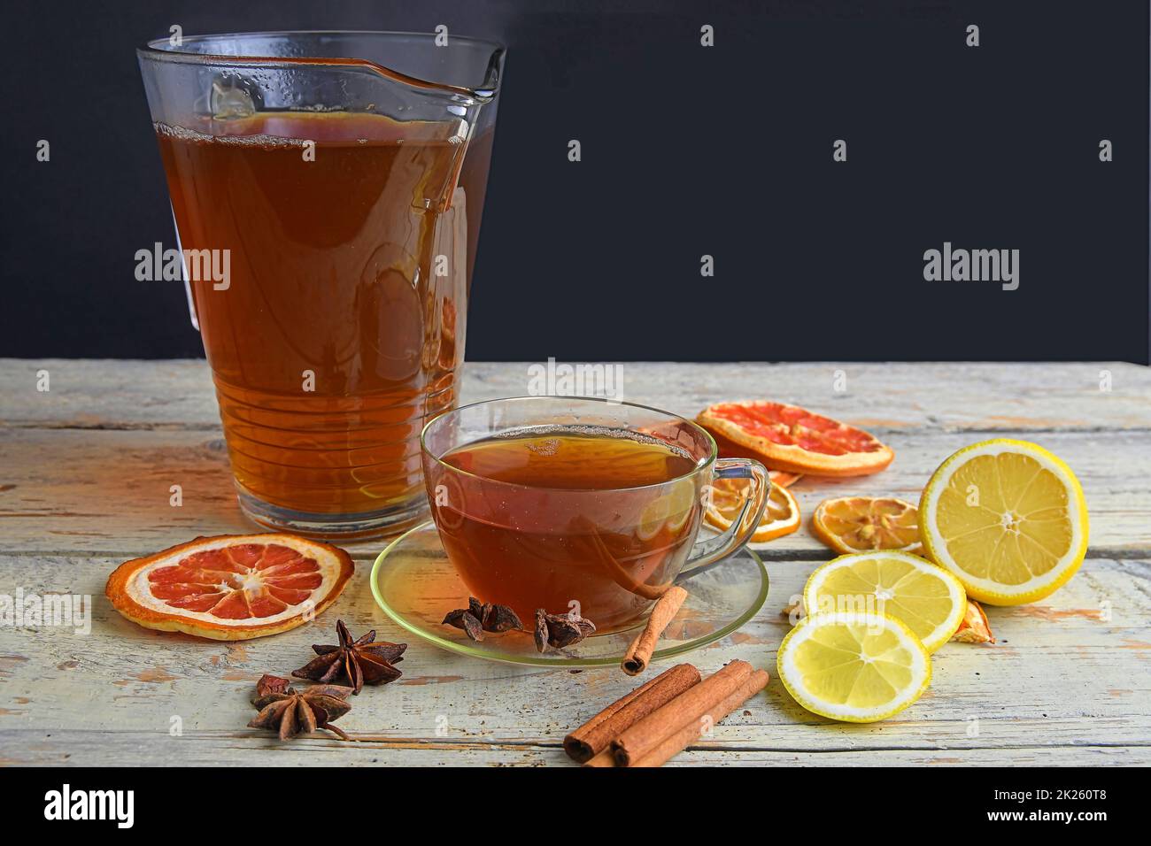 Tasse de thé noir en verre avec bâtonnets de cannelle, étoile anisée, citron et fruits secs sur fond de table en bois blanc.Verseuse de thé noir.Grand espace de copie Banque D'Images