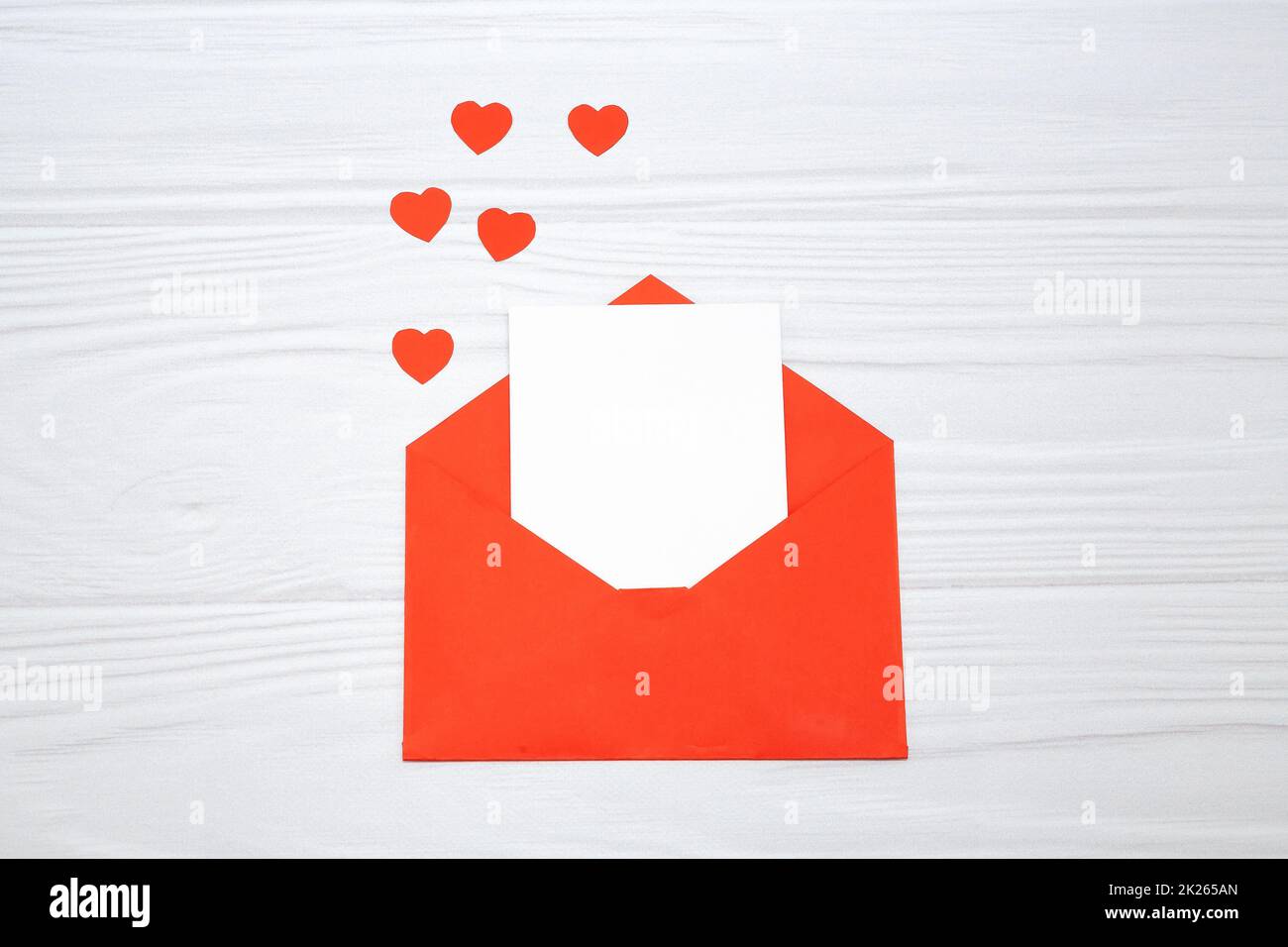 Enveloppe rouge avec une feuille de papier blanche et des coeurs rouges sur fond blanc en bois. Banque D'Images