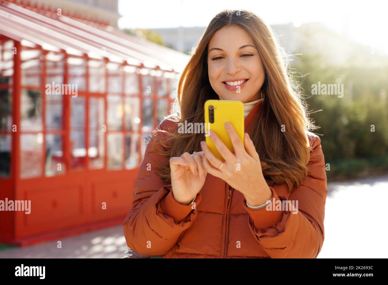 Belle femme souriante dans une veste bouffante tenant un smartphone en hiver Banque D'Images