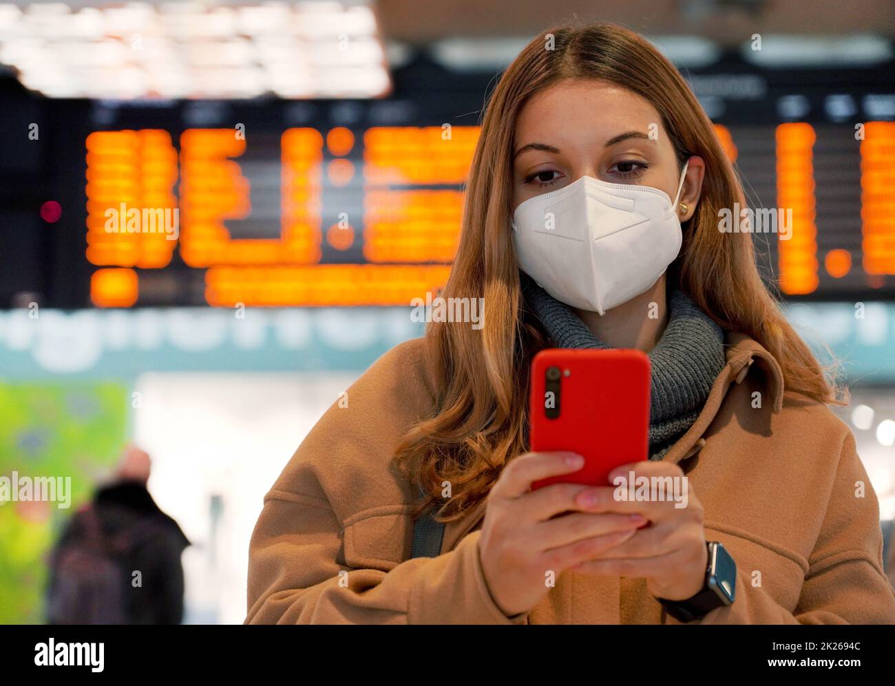 Portrait d'une femme portant un masque médical utilisant un smartphone avec passeport sanitaire pendant une pandémie et tableaux d'horaires en arrière-plan Banque D'Images