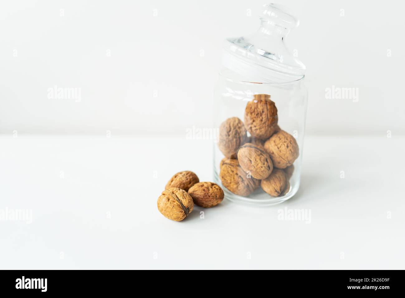 De beaux noyaux de noyer dans un pot en verre, des noix entières dans la coquille peuvent être vues à proximité, sur une table blanche. Le concept de stockage approprié des noix. Mise au point sélective. Banque D'Images