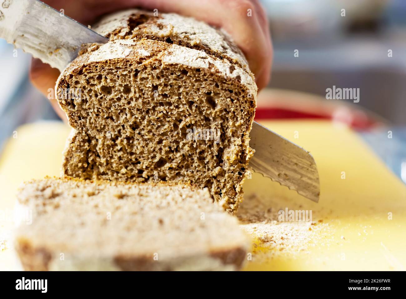 Trancher du pain de seigle frais avec un gros couteau dans une cuisine domestique Banque D'Images