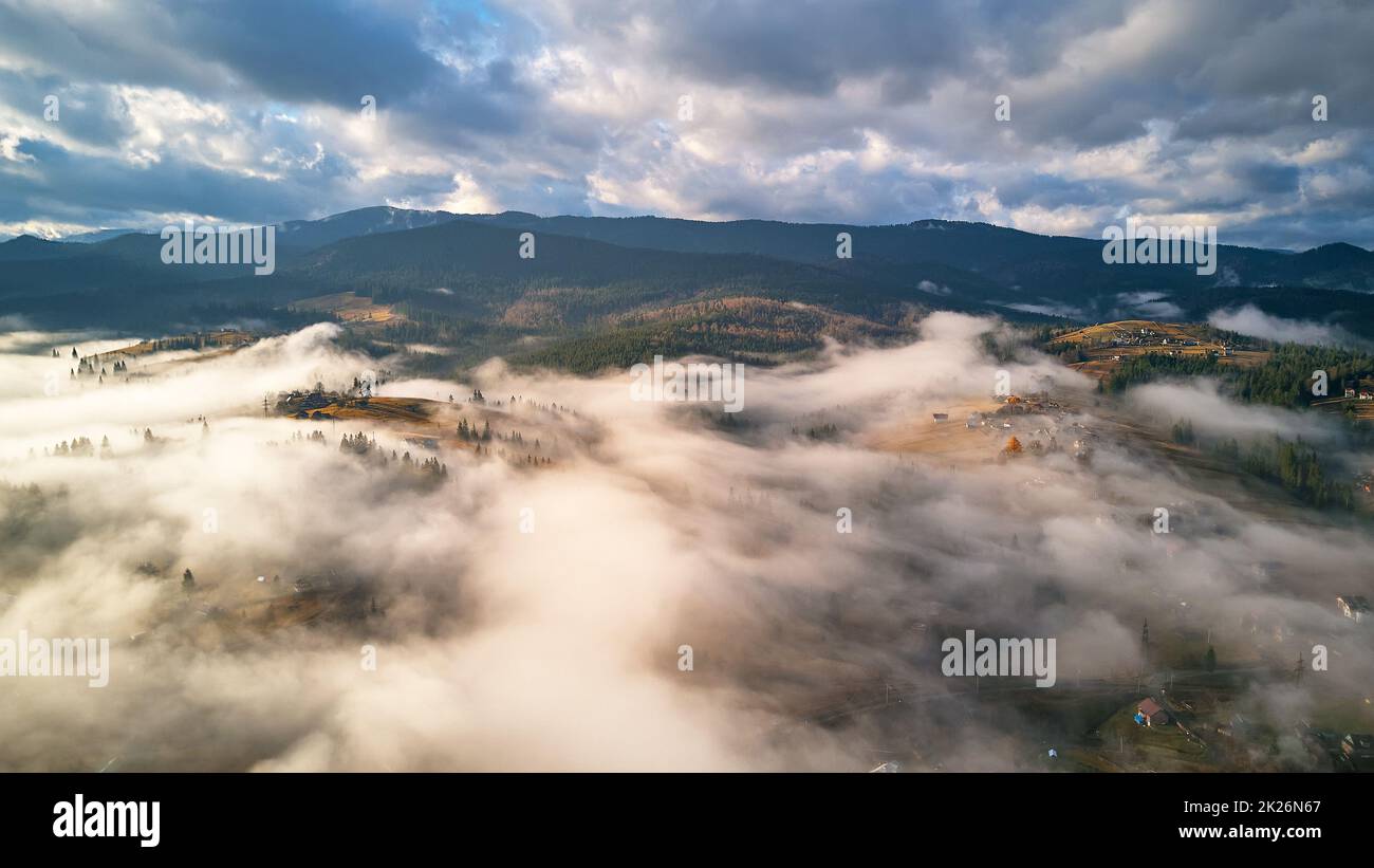Matin d'automne coloré au-dessus de la vallée de la montagne brumeuse. Village couvert de nuages bas. Paysage rural d'automne. Brumeux froid en novembre matin Banque D'Images