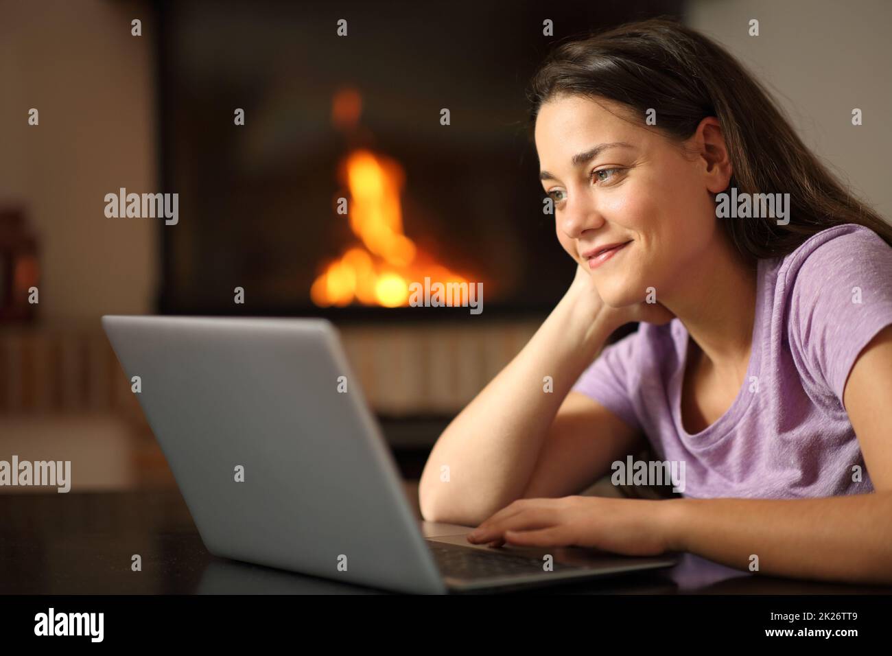 Femme vérifiant un ordinateur portable à la maison avec une cheminée Banque D'Images