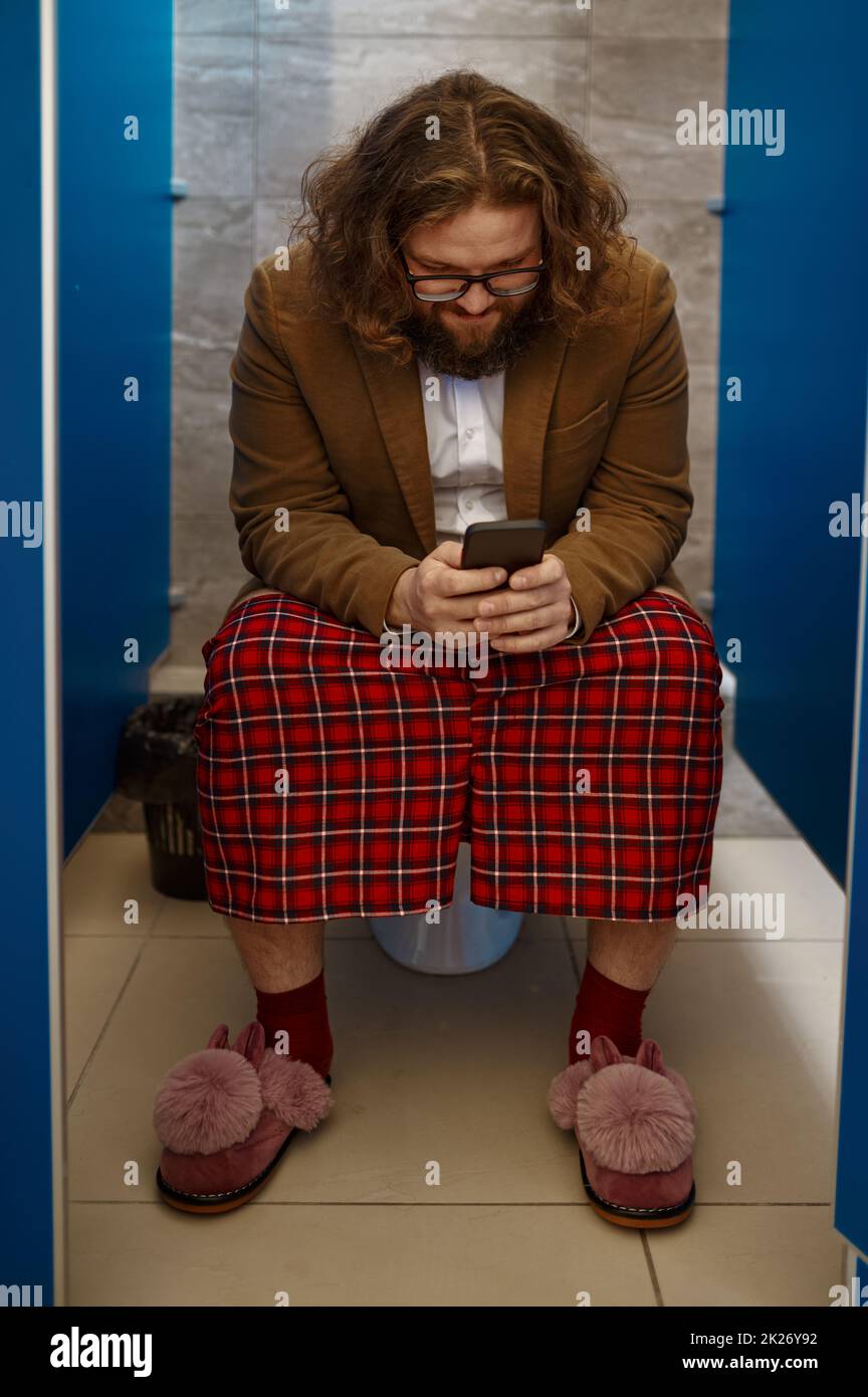 Homme d'affaires utilisant son téléphone tout en étant assis sur les toilettes Banque D'Images