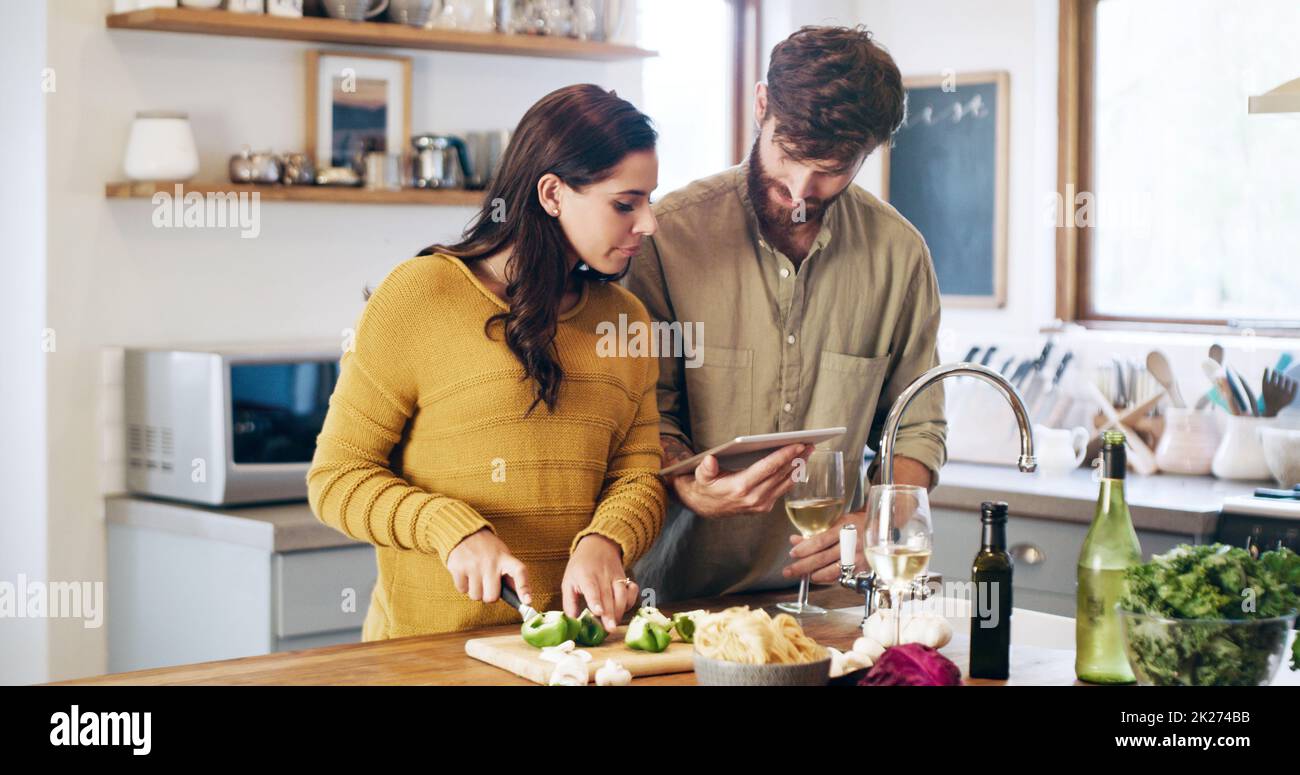 Le travail d'équipe fait fonctionner la recette.Prise de vue d'un jeune couple à l'aide d'une tablette numérique tout en préparant un repas à la maison. Banque D'Images