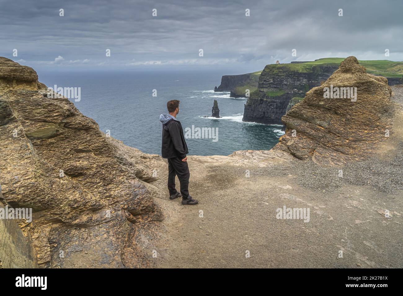 Homme debout au bord des falaises emblématiques de Moher, Wild Atlantic Way, Irlande Banque D'Images