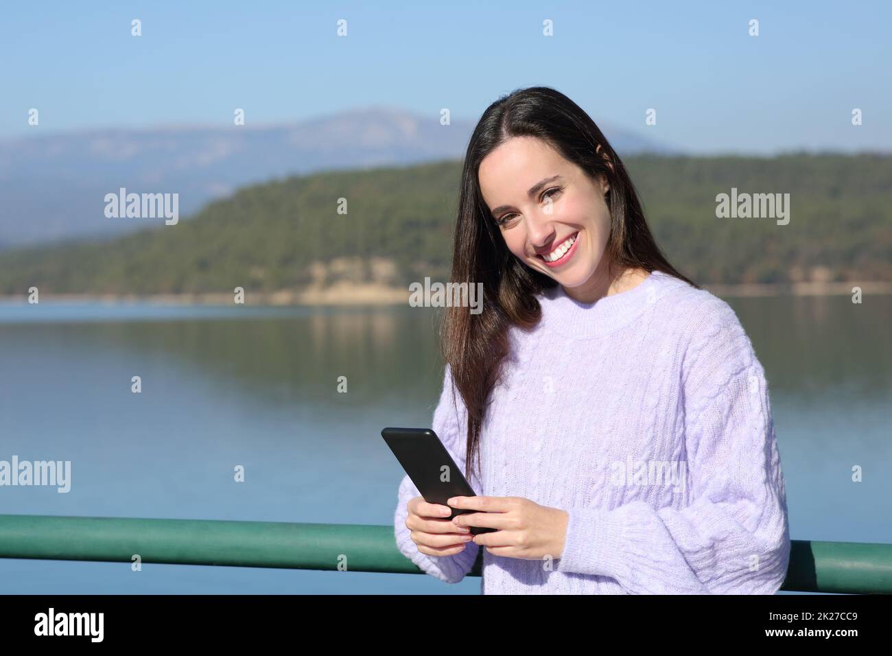 Une femme heureuse tient le téléphone et regarde l'appareil photo dans un lac Banque D'Images