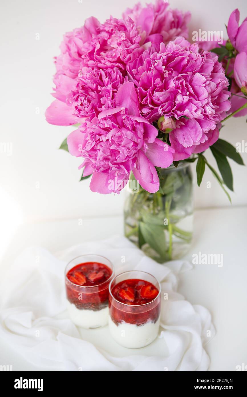 Un beau bouquet de pivoines roses dans un vase sur une table blanche est accompagné d'un dessert de fraise en forme de coeur. Saint-Valentin, 8 mars. Banque D'Images