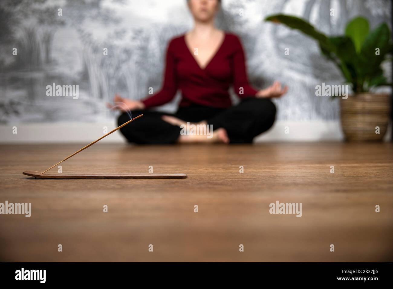 Femme consciente méditant à la maison avec des bâtons d'encens brûlants, se sitant dans la pose de lotus. Tenir les mains sur les genoux avec les paumes orientées vers le haut. Banque D'Images