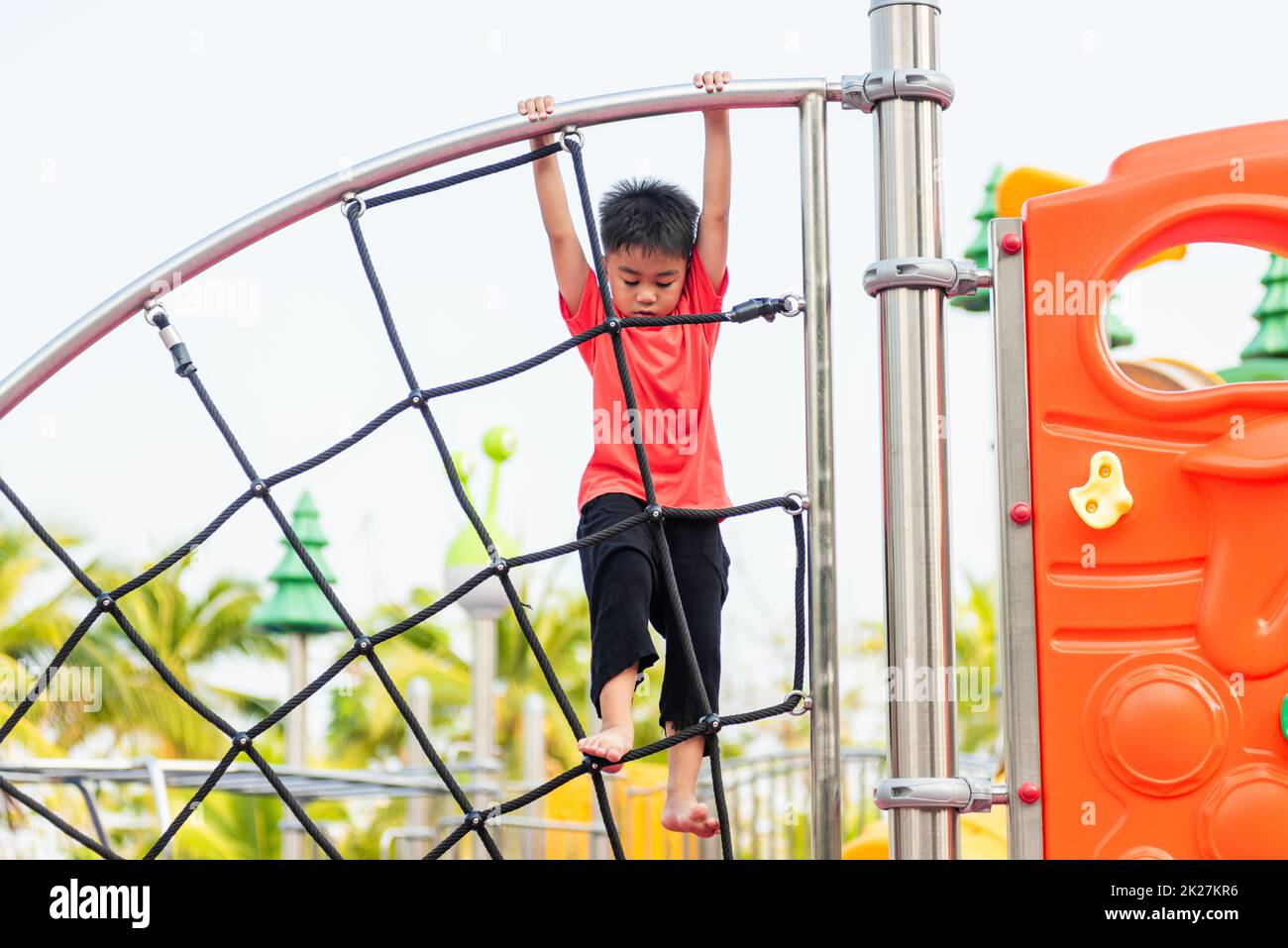 Enfant asiatique souriant jouant à l'escalade sur le terrain de jeu extérieur Banque D'Images