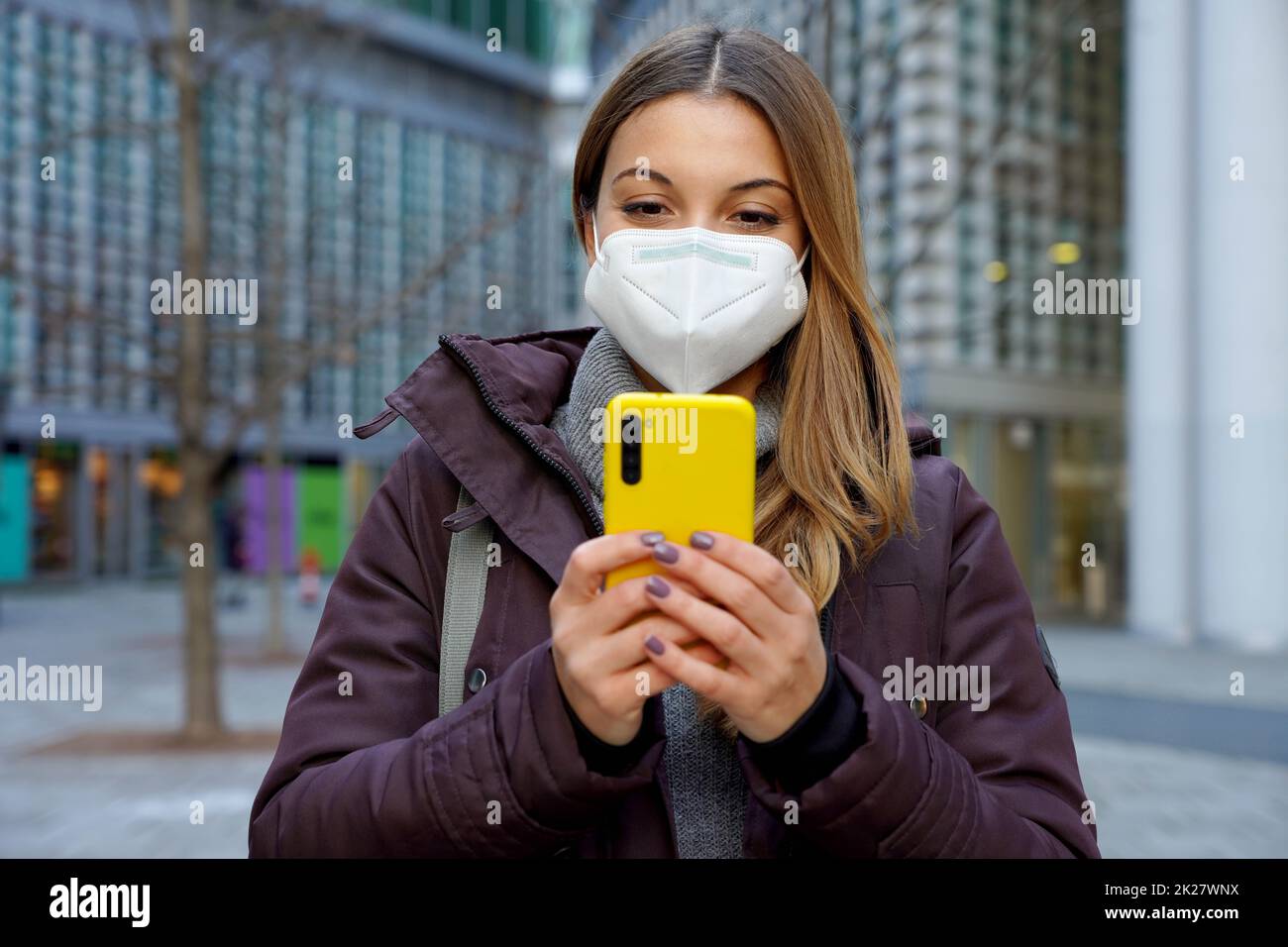 Vue de face de la femme d'hiver avec FFP2 KN95 masque de protection discutant avec un smartphone dans la rue de la ville Banque D'Images