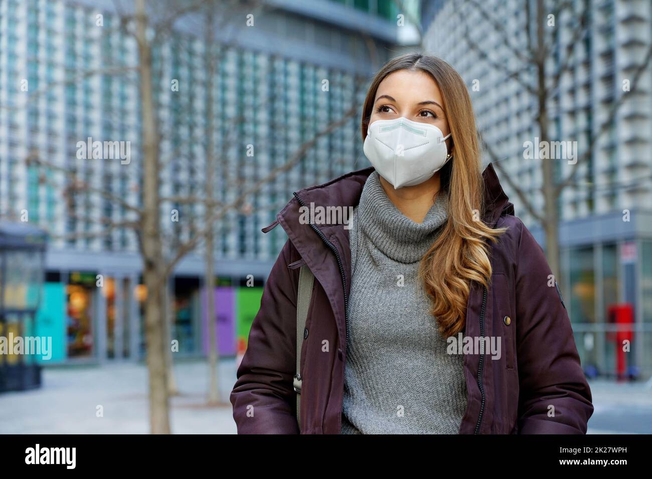 Photo moyenne d'une belle femme portant un masque protecteur marchant dans la rue de la ville en vêtements d'hiver Banque D'Images