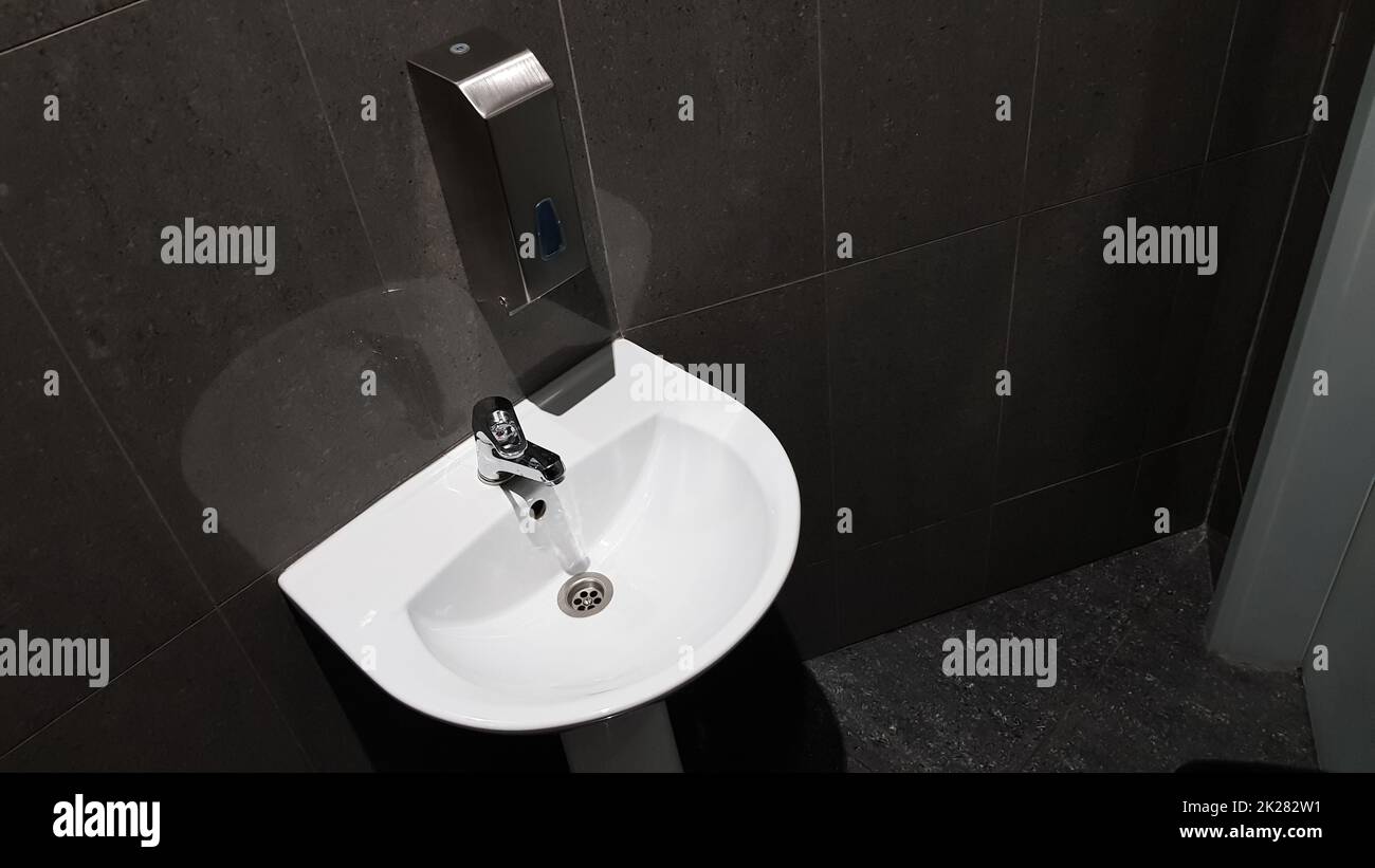 lavabo en céramique blanche avec robinet en chrome dans les toilettes avec carreaux gris Banque D'Images