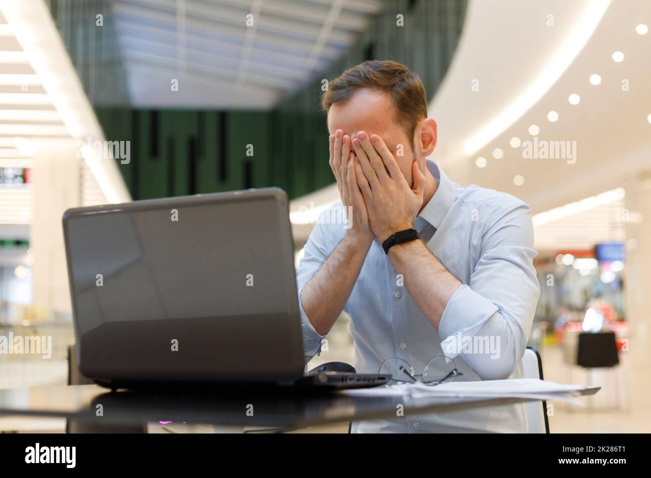 Je me sens fatigué. Un jeune homme frustré se couvrant le visage avec les mains tout en travaillant sur un ordinateur portable Banque D'Images